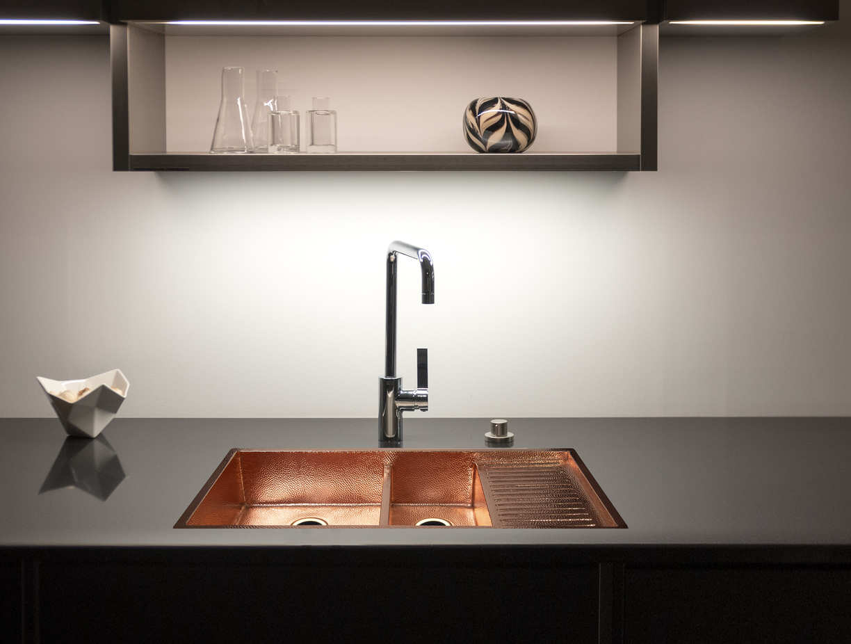 Modern kitchen with copper sink and black faucet against a neutral wall.